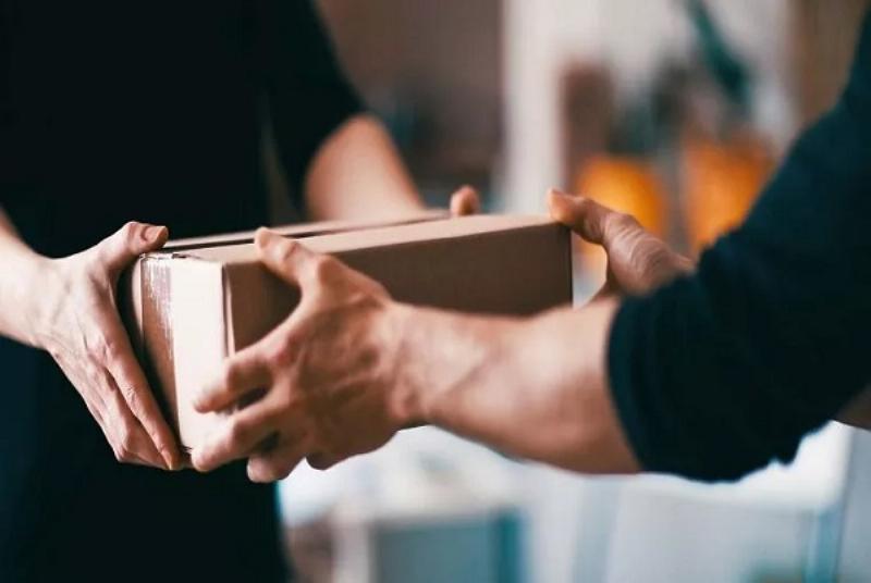Một hộp carton nhỏ với nhãn địa chỉ viết tay hoặc in, có dòng mã bưu chính được ghi rõ